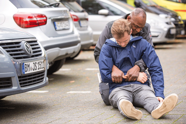 Eine bewusstlose Person wird mittels dem Rettungsgriff von der Straße gezogen. 