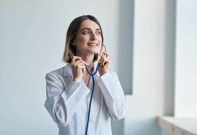 Woman with professional stethoscope Doctor in medical gown in bright room